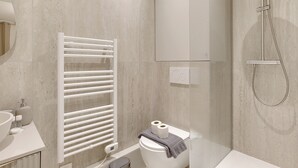 A modern bathroom with a white toilet, a glass shower enclosure, and a white towel rack. - Appartements rue Garnier (Neuilly-sur-Seine)