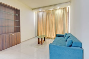 A living room with a blue sofa, a glass table, and a wooden cabinet. - Fabhotel Destination 41 (Pune)