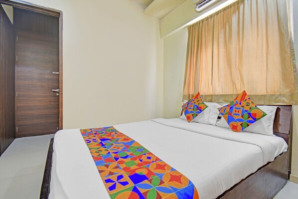 A neatly made bed with a colorful geometric-patterned bedspread and pillows, a wooden wardrobe, and a window with sheer curtains. - Fabhotel Destination 41 (Pune)