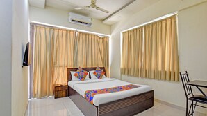 A bedroom with a bed, curtains, a ceiling fan, an air conditioner, and a desk with a chair. - Fabhotel Destination 41 (Pune)