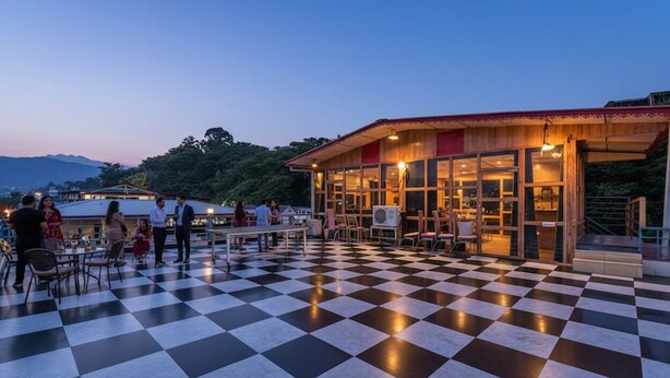 A checkered outdoor area with tables and chairs, a building with large windows, and a view of the mountains in the background.