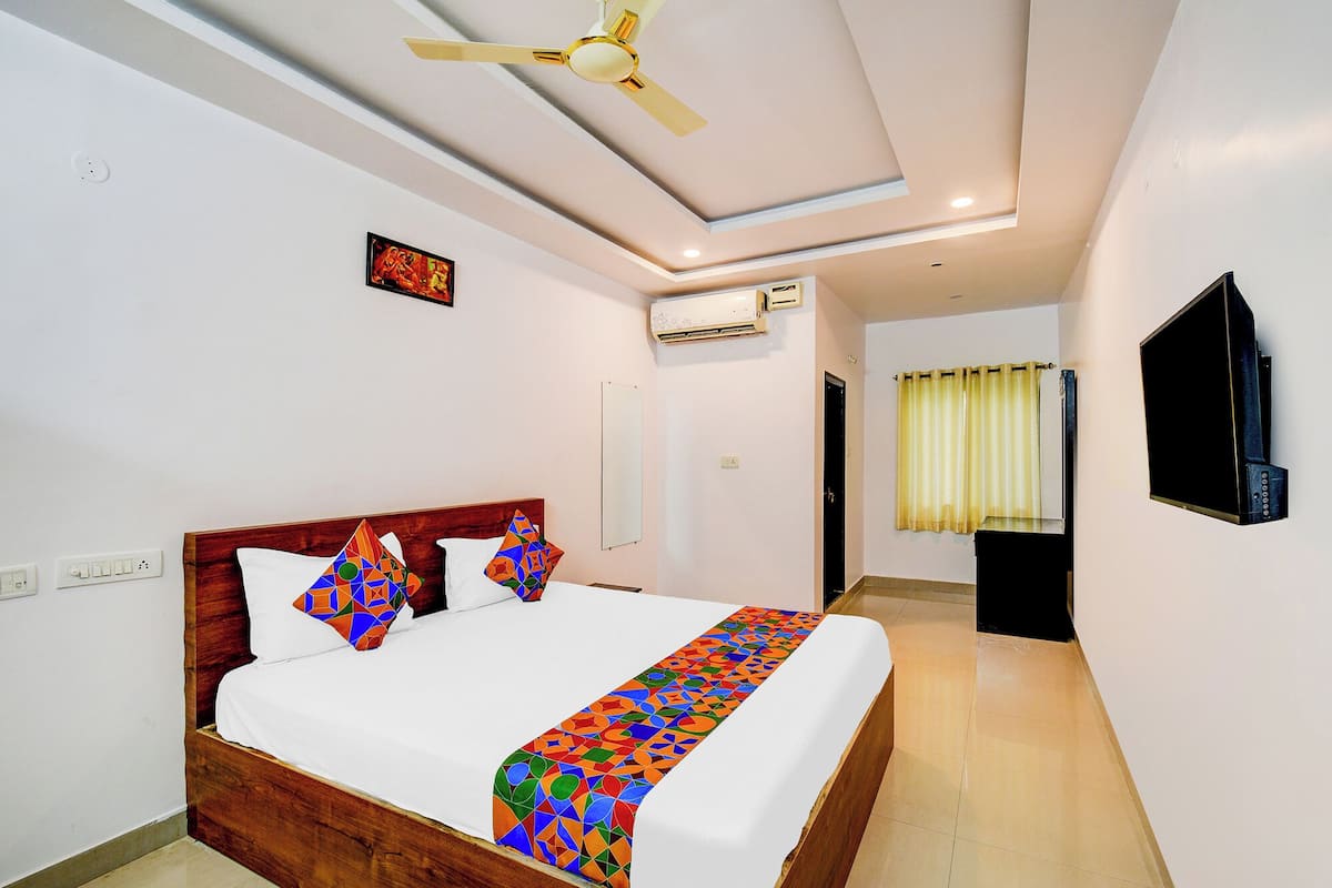 Hotelkamer met een bed, een plafondventilator, een airconditioning, een televisie en een badkamer met douchegordijn.