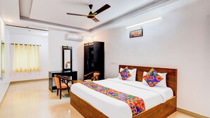 A hotel room with a large bed, a desk, a chair, a ceiling fan, and a painting on the wall. - Fabhotel Pushpa Grand (Hyderabad)