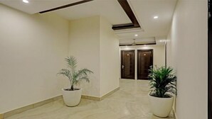 Un couloir avec deux plantes en pot, un ventilateur de plafond et, au fond, une porte à deux battants.