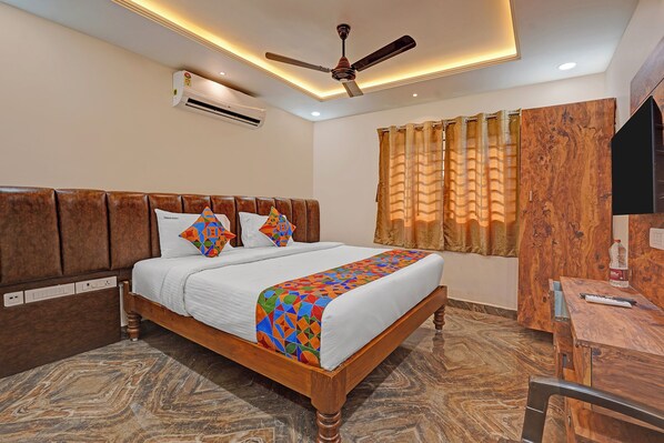 A hotel room with a wooden bed, a ceiling fan, an air conditioner, a window with curtains, and a desk with a chair. - Fabhotel Pranavam Residency (Tirupati)