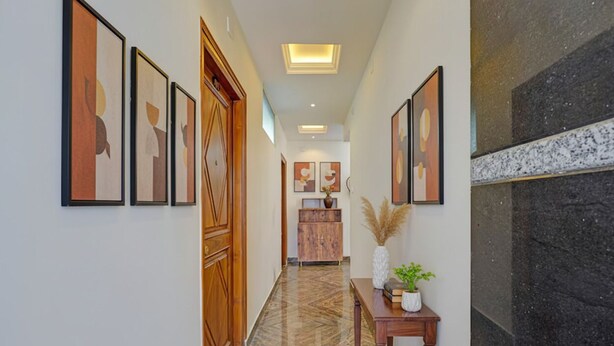 Un pasillo con obras de arte enmarcadas, una puerta de madera, suelo de mármol y una pequeña mesa con una planta.
