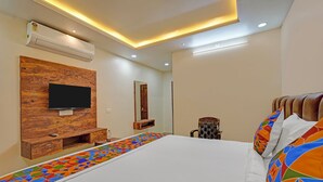 Habitación de hotel moderna con una cama grande, cabecero de madera, televisor de pantalla plana montado sobre un panel de madera, mesita de noche con una botella y un corredor con motivos geométricos de colores.