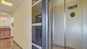 Un pasillo con mostrador de recepción, extintor en la pared y puerta metálica de ascensor.