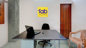 Een vergaderruimte met een zwarte tafel, twee stoelen, een laptop en een afstandsbediening. Een houten deur en een geel bord met 'fab hotels' zijn zichtbaar.