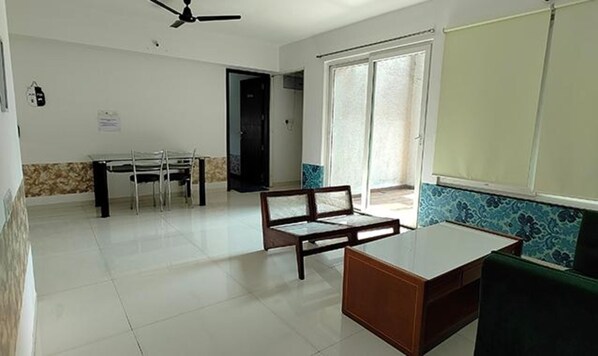 A room with a dining table, chairs, a sofa, a ceiling fan, and a window with a view. - Fabhotel Ekab Hospitality (Pune)