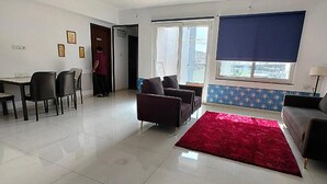 A spacious living room with a dining area, a red rug, and a large window with blinds. - Fabhotel Ekab Hospitality (Pune)