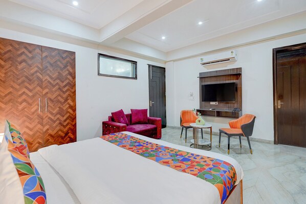 A hotel room with a bed, a sofa, two chairs, a TV, and an air conditioning unit. - Fabhotel Rush Residency (Noida)