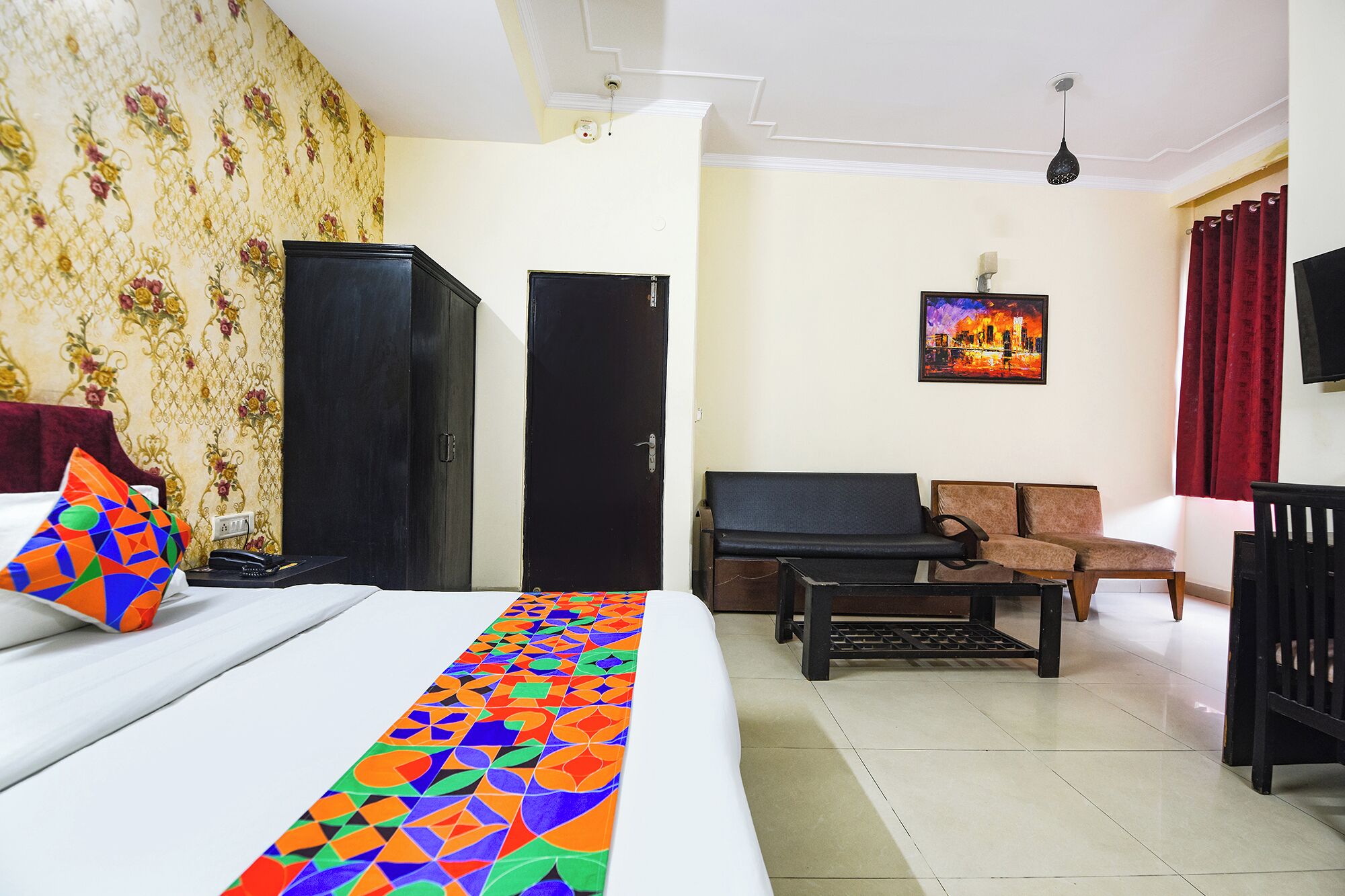 A hotel room with a bed, a desk, a chair, a wardrobe, and a painting on the wall.