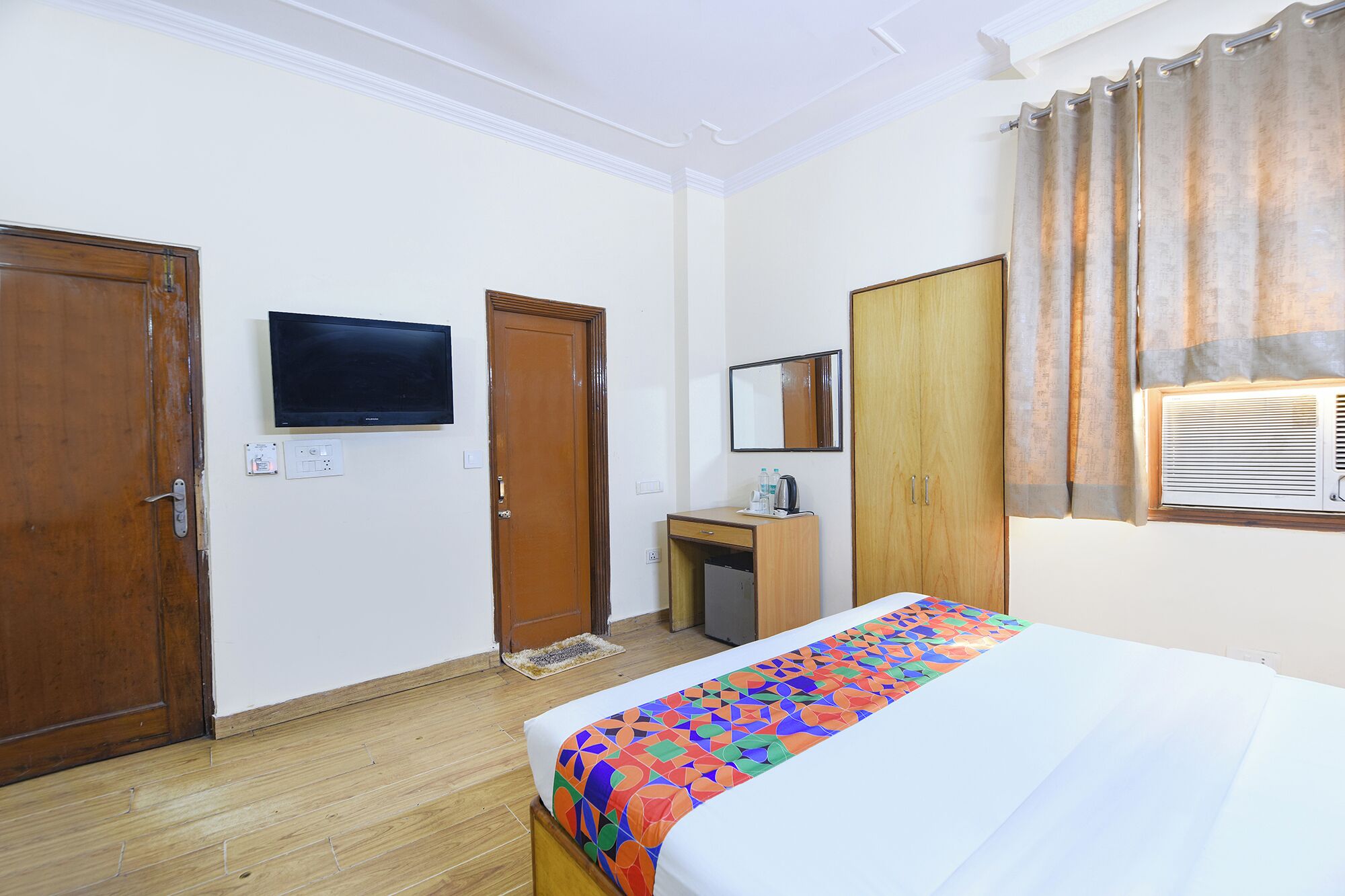 A hotel room with a bed, a desk, a television, a mirror, and a window with curtains.