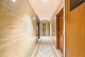 A corridor with marble walls, a tiled floor with yellow lines, and a wooden door with a number plate. - Fabhotel Ashoka International (New Delhi)