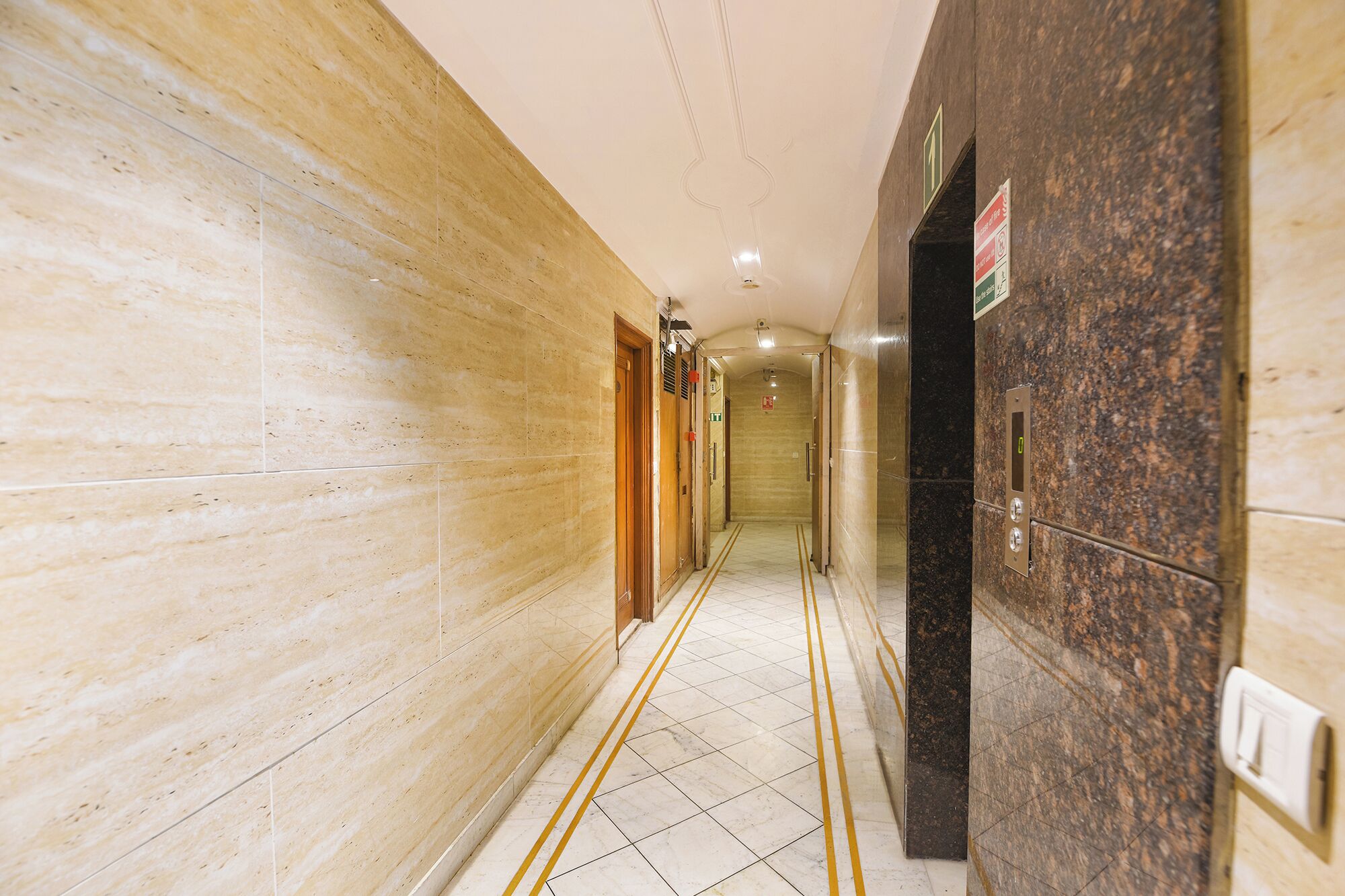 A hallway with marble walls, a tiled floor, and a door with a sign.
