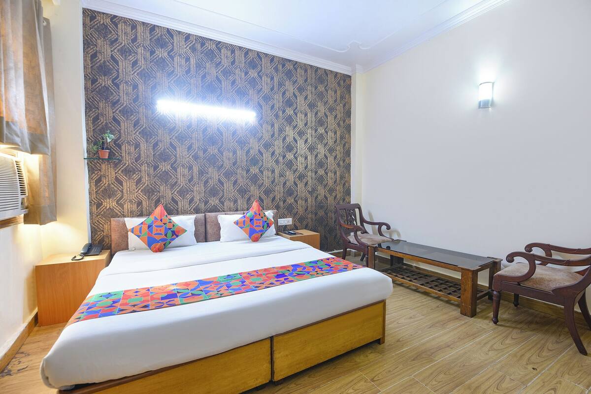 Een hotelkamer met een bed, een bureau, twee stoelen, een potplant en behangpapier met een patroon.