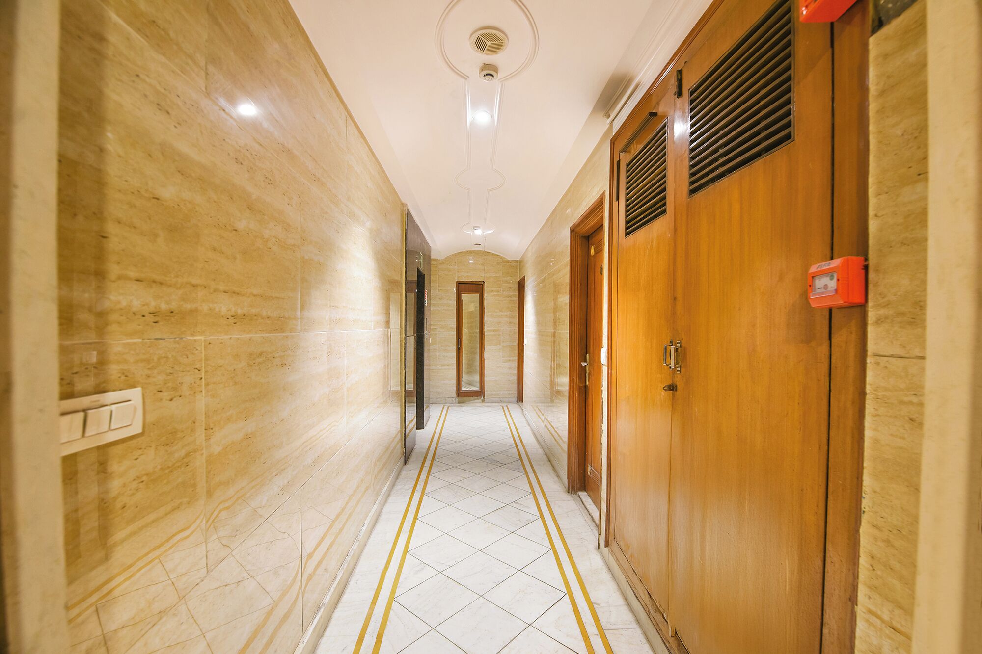 A hallway with marble walls, wooden doors, and a tiled floor with yellow lines.