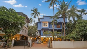 A multi-story building with a blue facade, surrounded by palm trees and greenery. - Fabhotel 22 Square Living Spaces (Calangute)