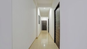 A long, narrow hallway with white walls and a shiny tiled floor, leading to a door at the end. - Fabhotel Aakarshan Residency (New Delhi)