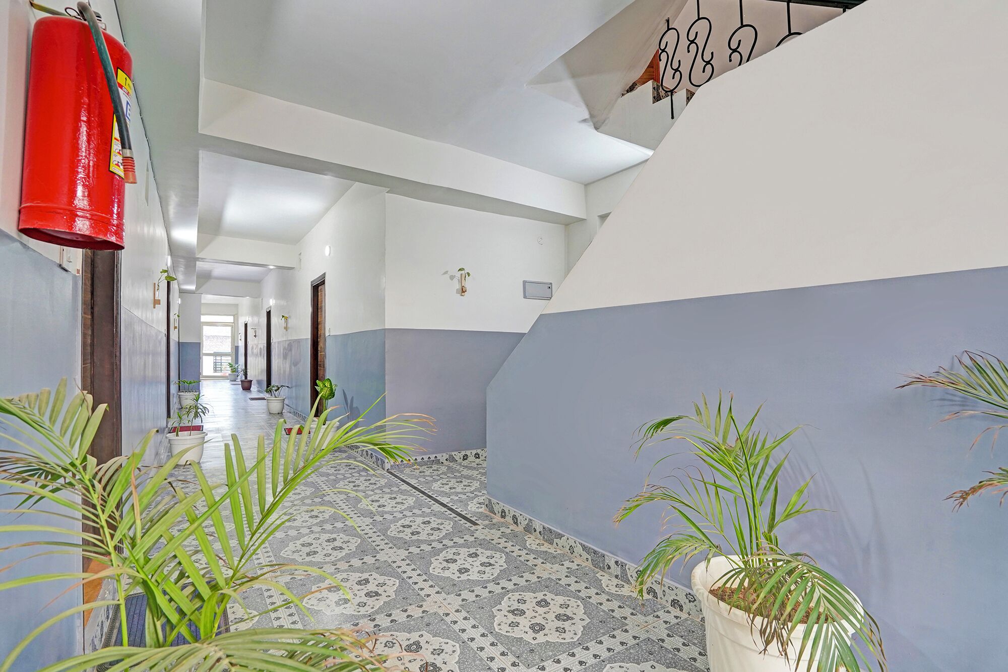 A hallway with patterned floor tiles, potted plants, and a red fire extinguisher.