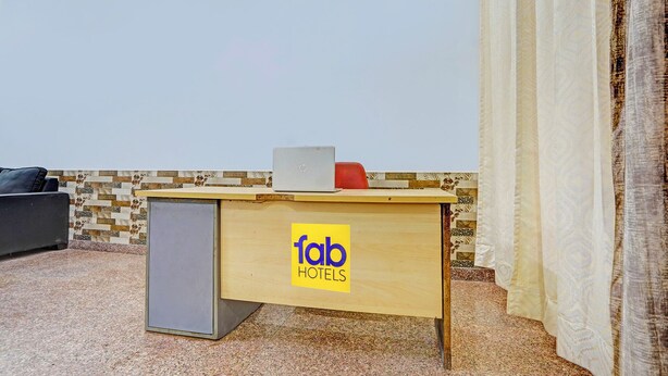 A small wooden desk with a laptop and a red object on top, a grey cabinet beside it, and a sign reading "fab hotels" on the desk. - Fabhotel Casa Residency (Noida)