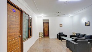 A hotel lobby with a reception desk, two sofas, a coffee table, and a wooden door with a glass panel. - Fabhotel Casa Residency (Noida)