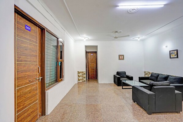 A hotel lobby with a reception desk, two sofas, a coffee table, and a wooden door with a glass panel. - Fabhotel Casa Residency (Noida)