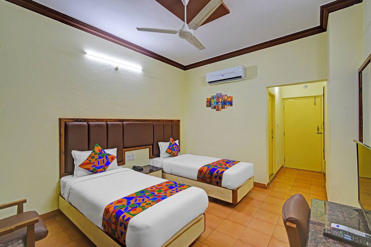 A hotel room with two beds, a ceiling fan, an air conditioning unit, a small table, and a chair.
