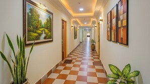 A hotel hallway with checkered flooring, framed artwork on the walls, and potted plants. - Fabhotel Ranjit Residency (Hyderabad)