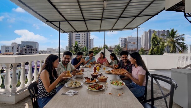 A group of people dining at an outdoor table with a view of city buildings and palm trees. - Fabhotel Ans Kp Annex (Pune)