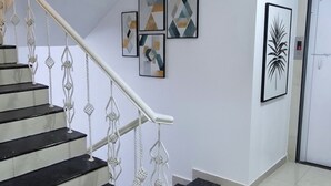 A staircase with white railings and black steps, leading to a room with a white door and a framed abstract painting on the wall. - Fabhotel Ans Kp Annex (Pune)