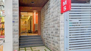 Una entrada de edificio con fachada de piedra, un letrero rojo y un área amurallada con portón metálico.