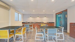 Comedor con varias mesas y sillas, cocina al fondo y una puerta con un letrero.