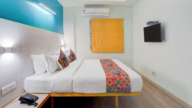 Habitación de hotel con cama, teléfono en la mesita de noche, unidad de aire acondicionado, televisor y ventana con cortina amarilla.