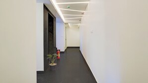 Un pasillo moderno con paredes blancas, suelo oscuro e iluminación empotrada en el techo.