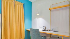 Una habitación pequeña y de colores vivos, con escritorio, silla y un refrigerador compacto.