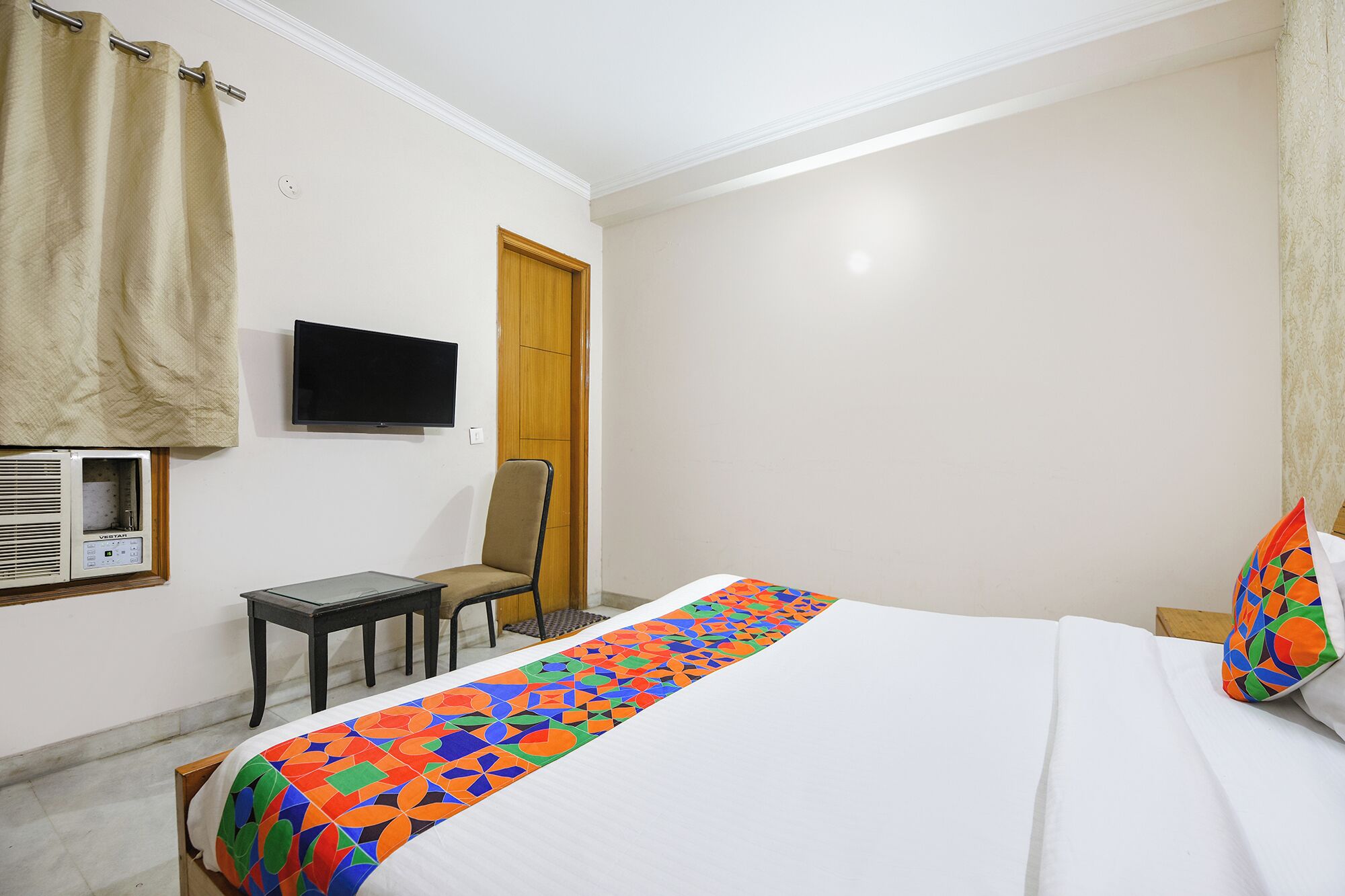 A hotel room with a bed, a TV mounted on the wall, a chair, and a heater.