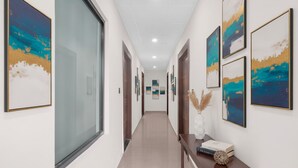 A hallway with framed artwork on the walls, a wooden console table with books and decorative items, and a large window on the left. - Fabhotel Yatri Nivas (Varanasi)