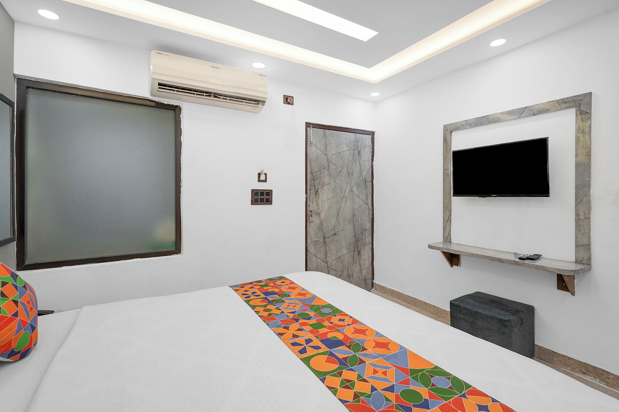 A modern hotel room with a large bed, a TV mounted on the wall, and a patterned rug.