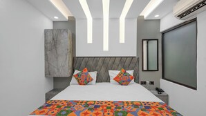 A modern bedroom with a large bed, geometric-patterned pillows, a marble accent wall, and recessed ceiling lighting. - Fabhotel Yatri Nivas (Varanasi)