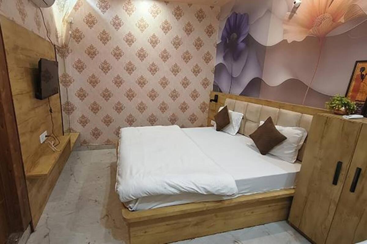 A bedroom with a wooden bed frame, white bedding, and a patterned wallpaper.