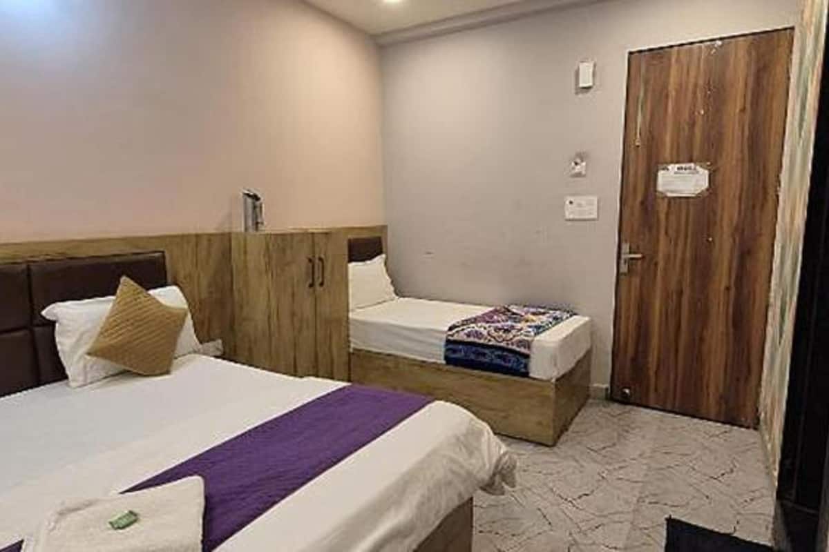 A hotel room with two beds, a wooden wardrobe, a door, and a tiled floor.