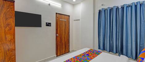 Un dormitorio con puerta de madera, cama blanca y cortina azul con un corredor de diseño geométrico y colores.