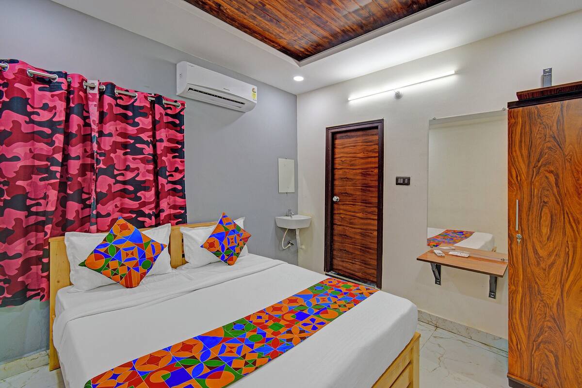 Un dormitorio con cama, armario de madera, mesita de noche con lámpara, espejo y baño con lavabo e inodoro.