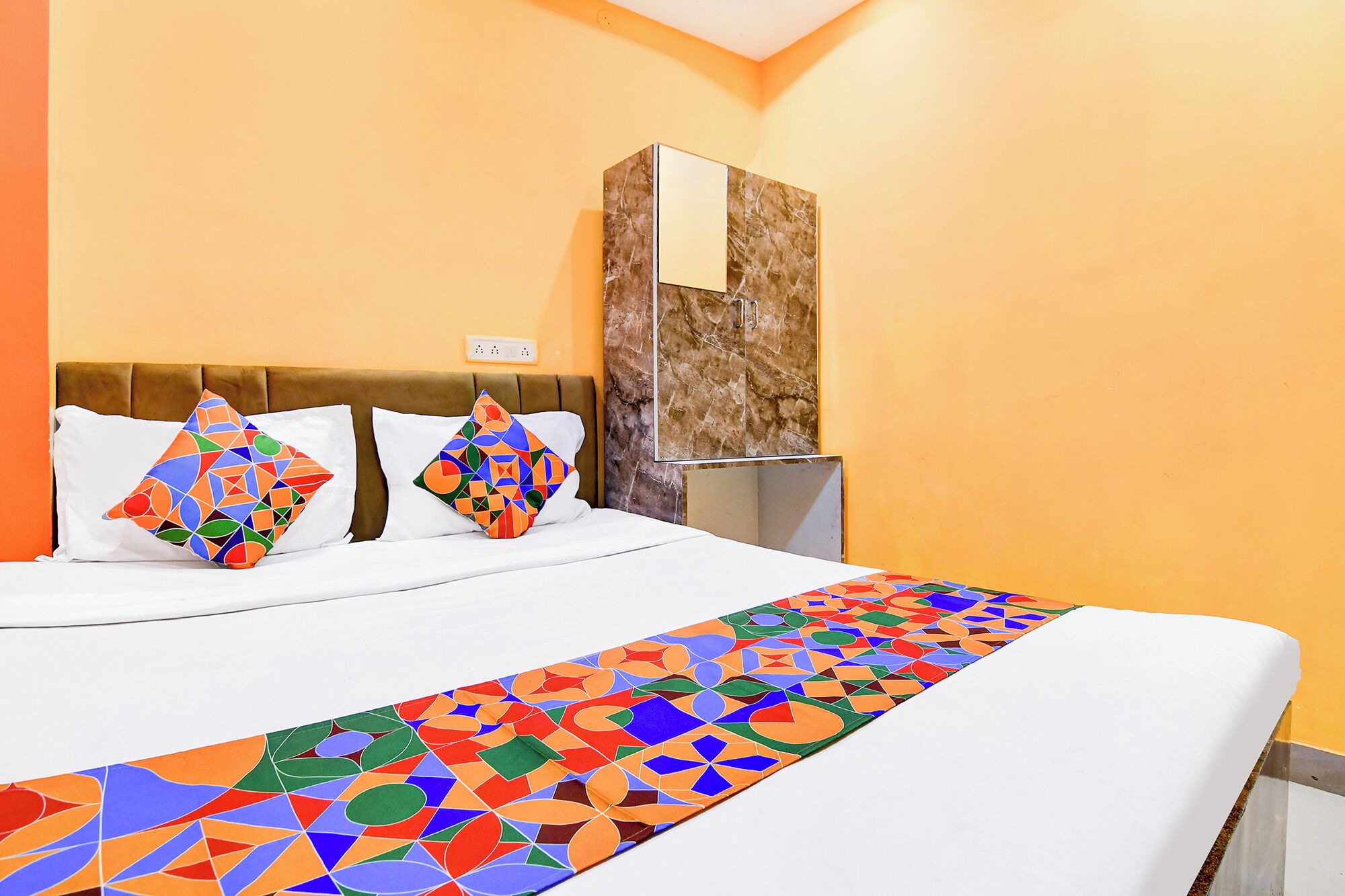 A hotel room with a bed, two pillows, a nightstand, and a marble cabinet.