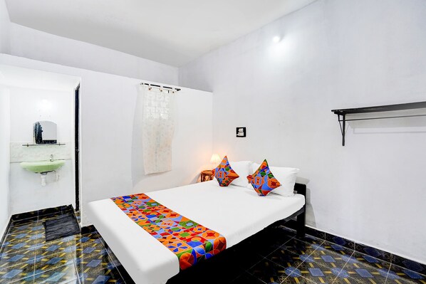 Habitación de hotel con cama, mesita de noche, lámpara, ventana con cortina, lavamanos y espejo.