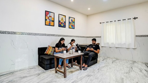 Un salon moderne avec un sol en marbre, un canapé noir, une table basse en bois et trois personnes assises, utilisant des appareils électroniques.