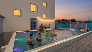 An indoor swimming pool with people enjoying the water, a covered seating area, and string lights. - Fabhotel Relax Inn (Shirur)