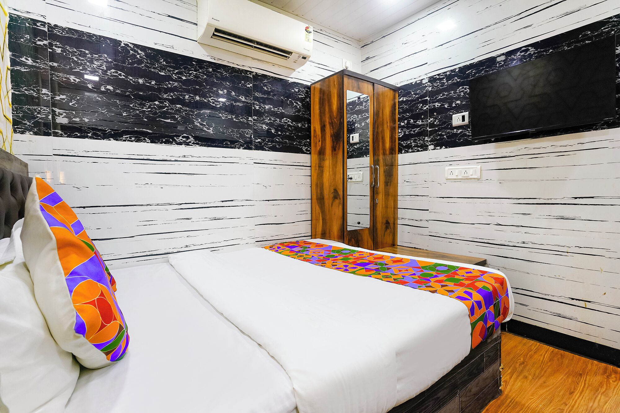 Una camera d'albergo con un letto, un armadio in legno, uno specchio e una televisione.